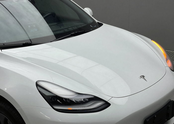 Clear PPF paint protection film installation on white sports car hood with orange accent lighting